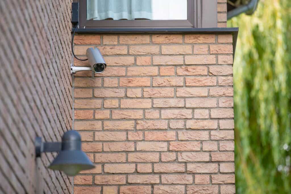 Wired cctv system positioned on the side of a brown brick house below a window