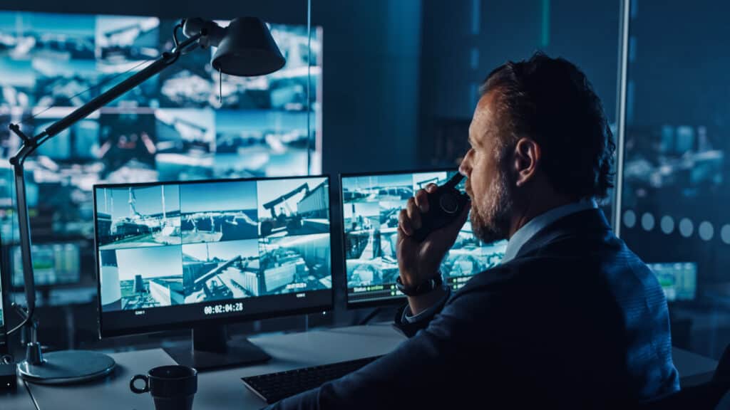 Man sat behind desk with multiple desktop screen displaying CCTV footage