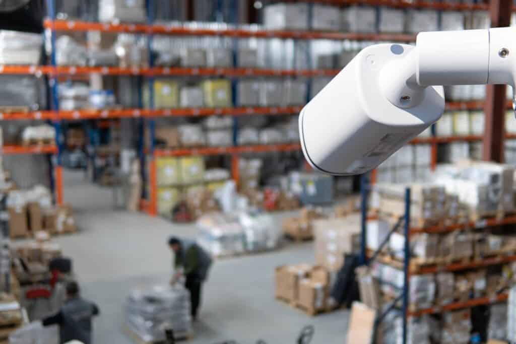 White CCTV camera overlooking warehouse floor with workers handling packages